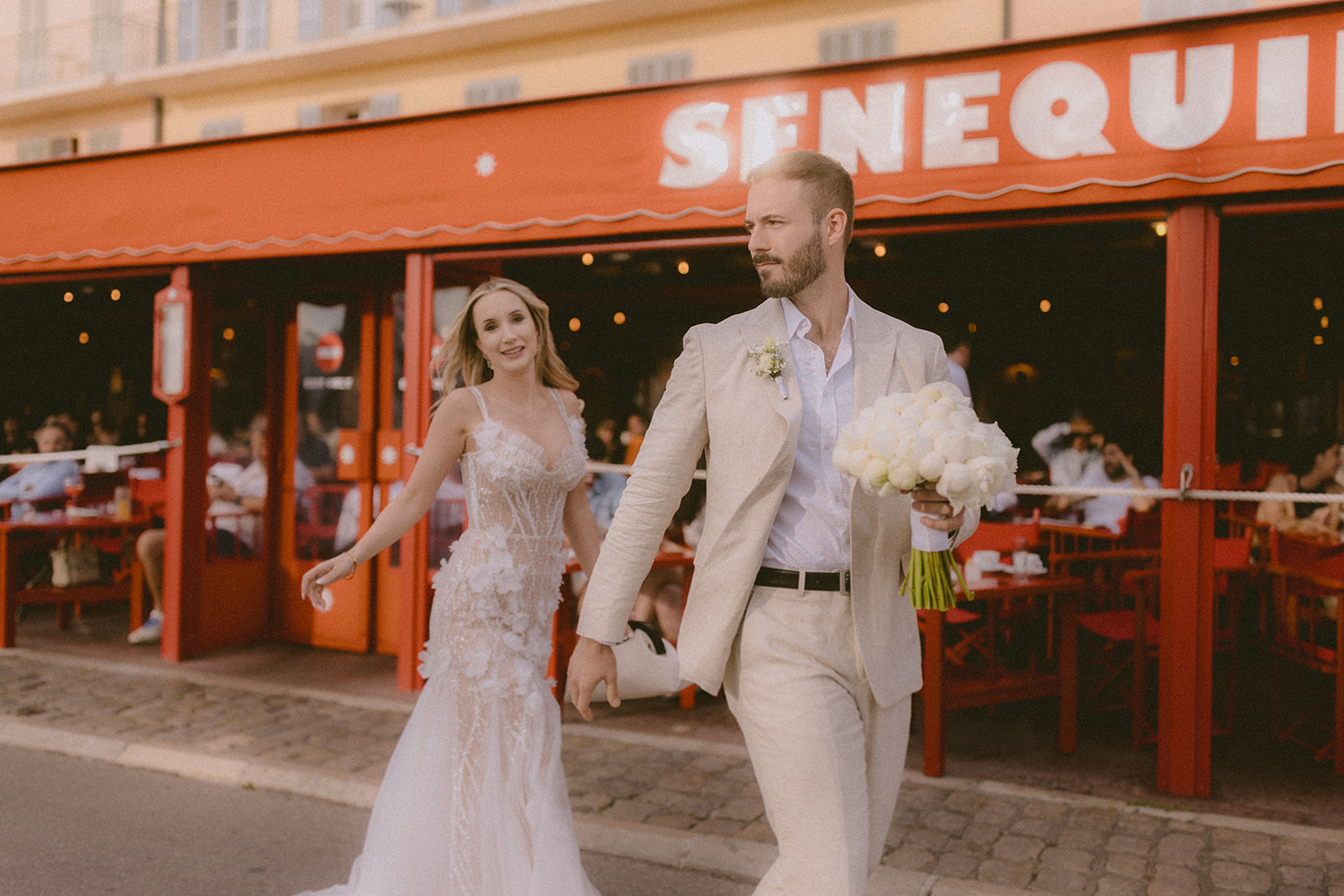 a couple walks in front of senequier, saint tropez